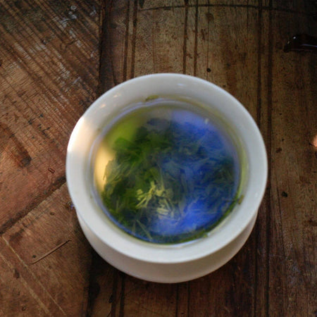 Flüssigkeiter Hochgebirgs-Wilder-Drachenbrunnen-Tee Grüntee in weisser Teetasse auf Holzoberfläche - Liquid High Mountain Wild Dragon Well Tea Green Tea in white teacup on wooden surface