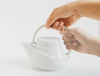 Zwei Hände halten RIDGE weisse Porzellan Teekanne Teegeschirr vor einem weissen Hintergrund - Two hands hold white porcelain teapot against a white background