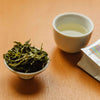 Loser blatt Tee in einer kleinen weissen Schale neben einer weissen Teetasse - Loose-leaf green tea in small white bowl near a white tea cup
