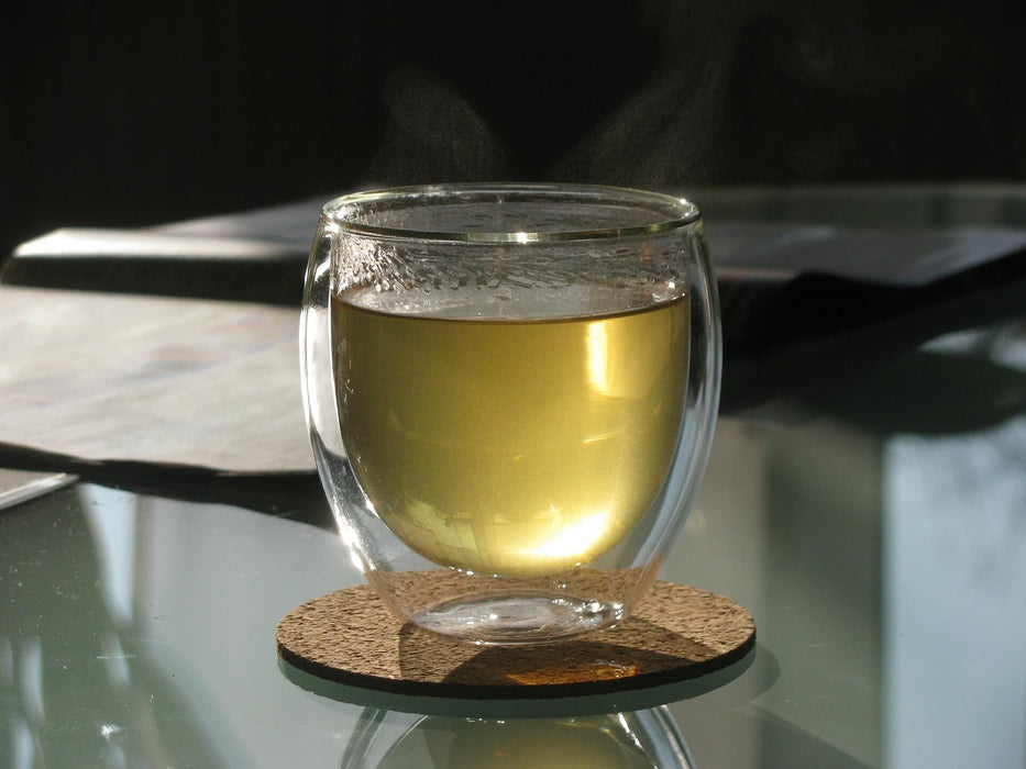 Flüssigkeit Loser blatt grüner Tee in transparenter Teetasse auf einer Glasfläche - Liquid loose-leaf green tea in transparent tea cup on a glass surface