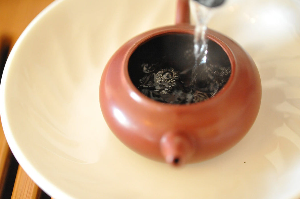 Keemun Maofeng loser blatt Schwarze Tee in brauner Teekane mit heissem Wasser übergossen auf grossem beigen Teller - Loose-leaf Black Tea  in large brown teapot on large beige plate