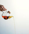 Hand giesst braunen flüssigen Tee aus transparenter Teekanne - hand pours brown liquid tea from transparent teapot