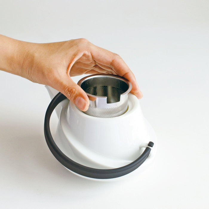 Hand hebt Edelstahl-Tee-Ei aus weisser Porzellan-Teekanne heraus - Hand lifts up stainless steel tea infuser from white porcelain teapot