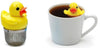 Tee-ei in Form einer Gummiente mit Edelstahl-Sieb neben Gummiente Tee-Aufgusskorb in einer weisse Tasse Tee auf weissem Hintergrund - Rubber duck tea infuser next to rubber-duck tea infuser in a white tea cup