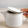 Hand halt weisse BRIM Teekanne auf Edelstahl Teegeschirr - Hand holds white BRIM stainless steel teapot teaware